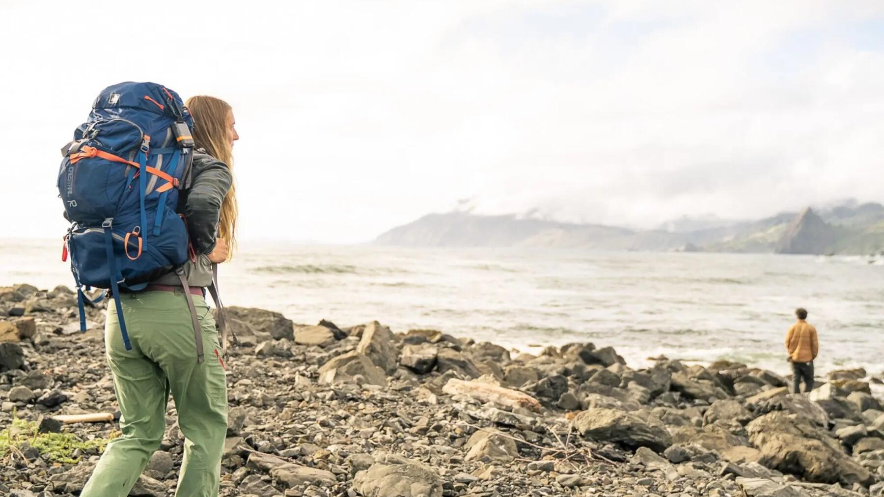Geocacher mit Wanderrucksack blickt von einem Aussichtspunkt auf ein anspruchsvolles Terrain