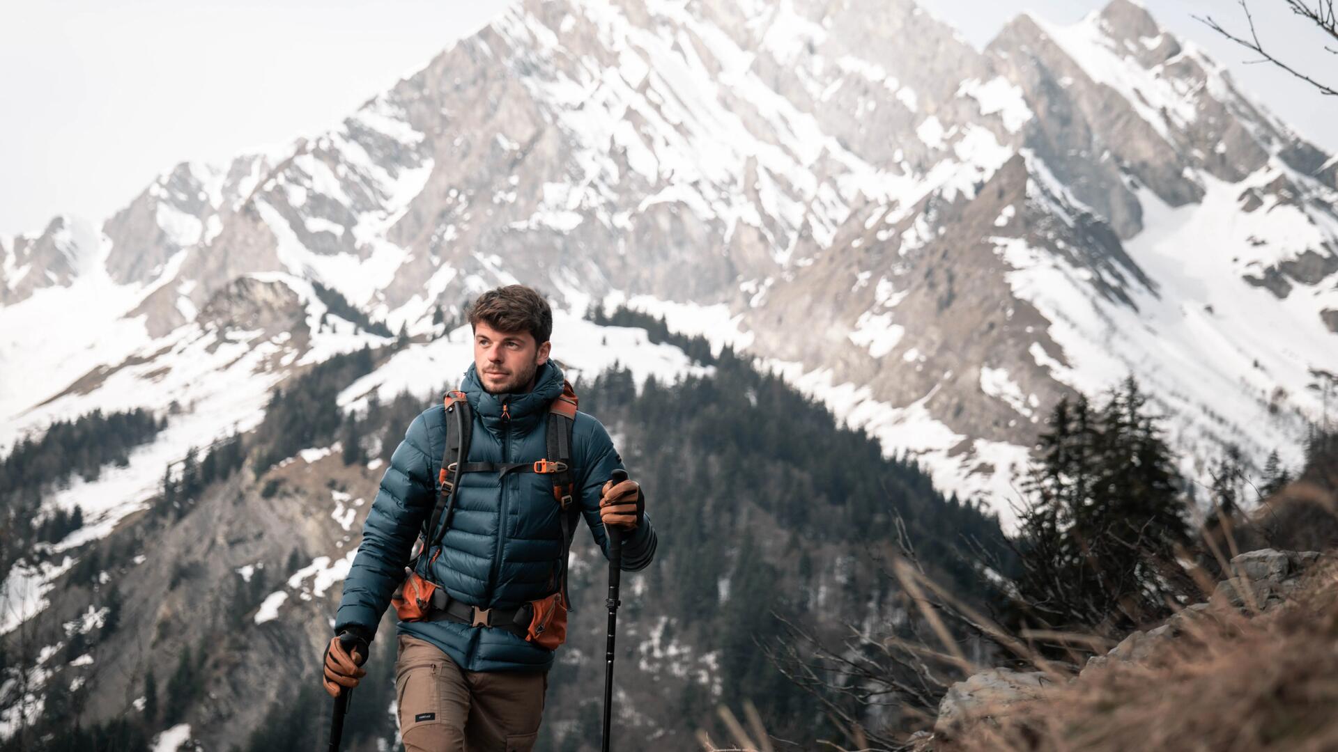 mężczyzna idący w górach z kijkami trekkingowymi 