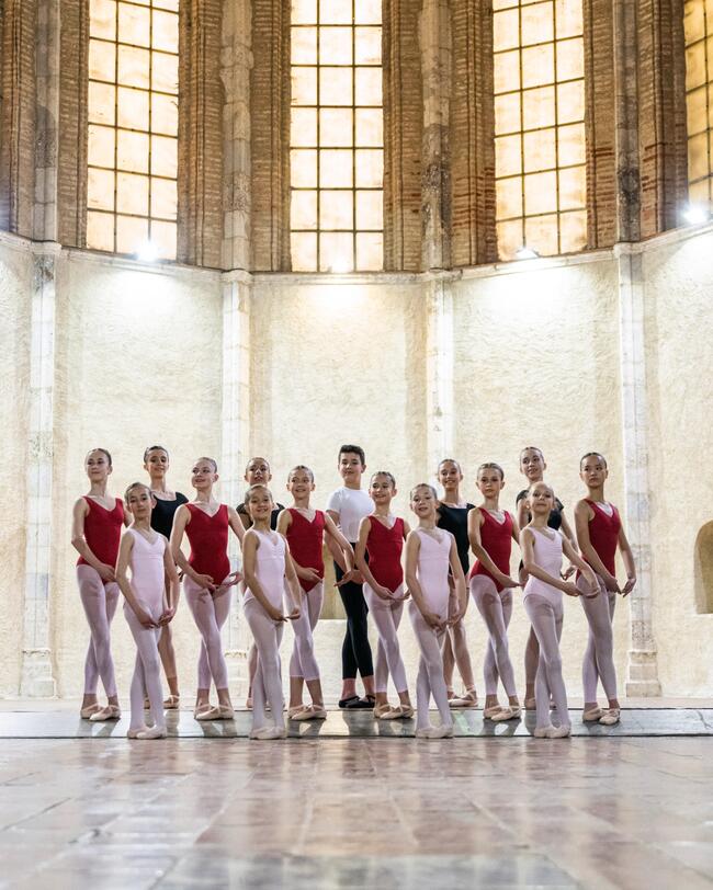 Eine Gruppe von Balletttänzer*innen steht in einem Saal..
