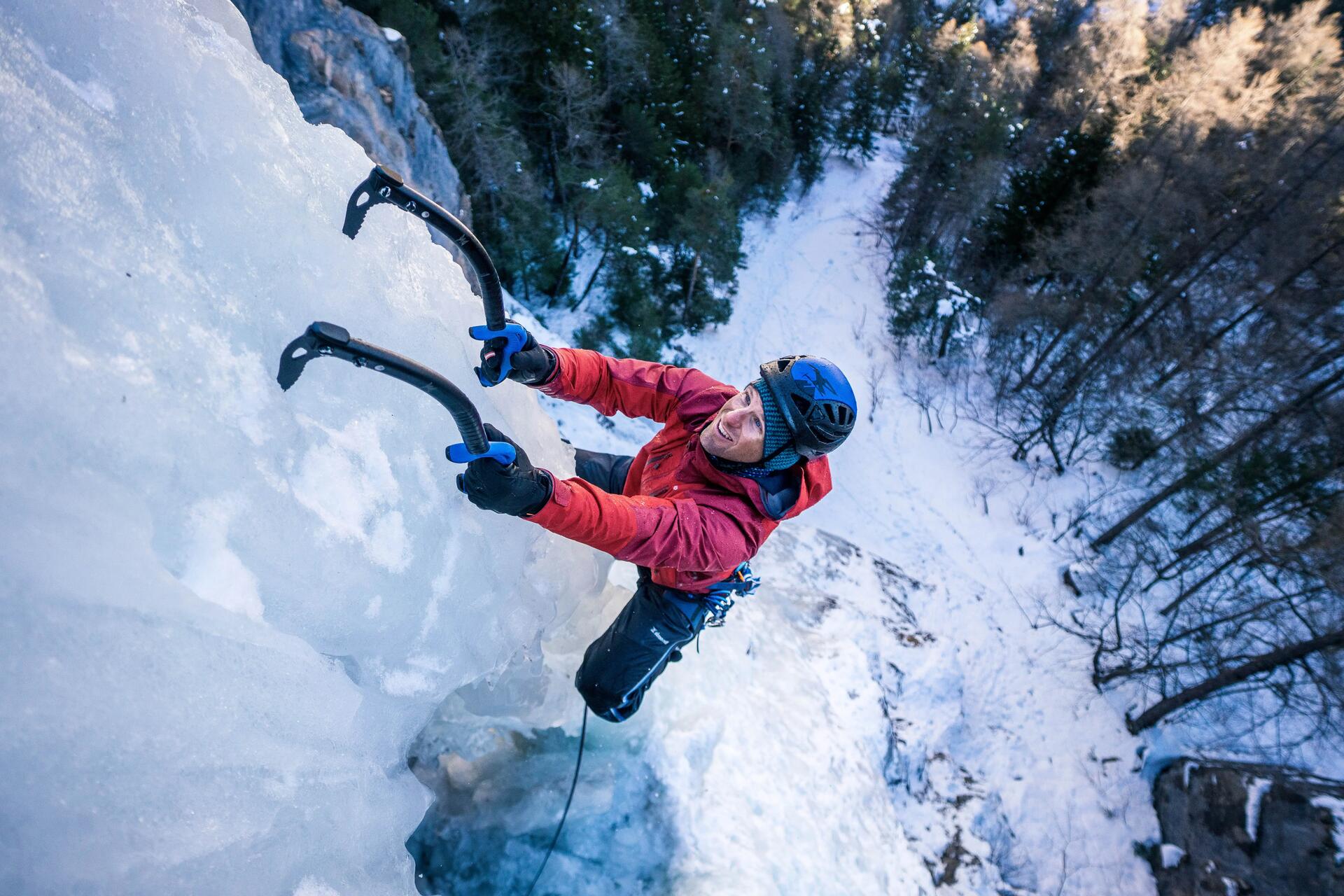 Mężczyzna w kasku i odzieży alpinistycznej wspinający się po lodzie z użyciem czekanów