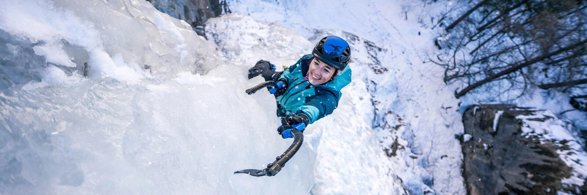 Kobieta w kasku wspinaczkowym wbijająca czekan w lód podczas wspinaczki lodowej