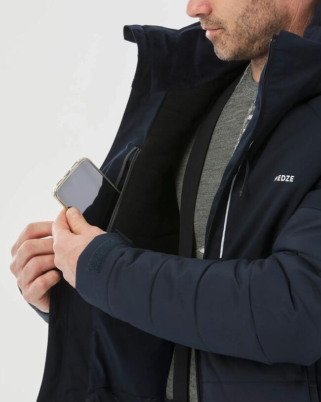 Nahaufnahme der Reißverschluss-Innentasche der Ski- und Snowboardjacke Herren 100 blau, in der gerade ein Handy verstaut wird.