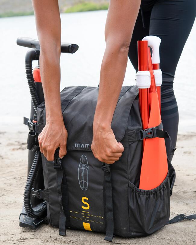Rucksack mit orangefarbenen Paddeln, schwarzes Material, gelbe Details, Handpumpe an der Seite, sandiger Hintergrund.