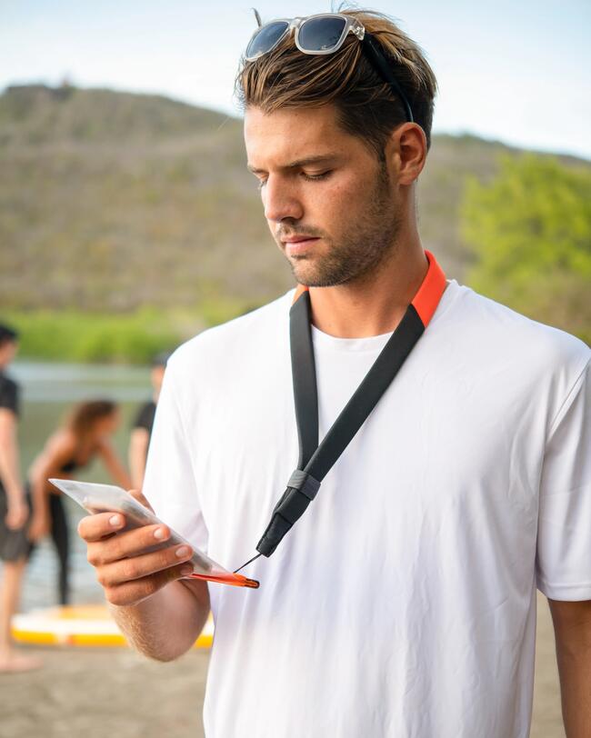 Mann in weißem T-Shirt, hält Smartphone, Hintergrund mit unscharfen Personen und grüner Natur, trägt Sonnenbrille auf Kopf.