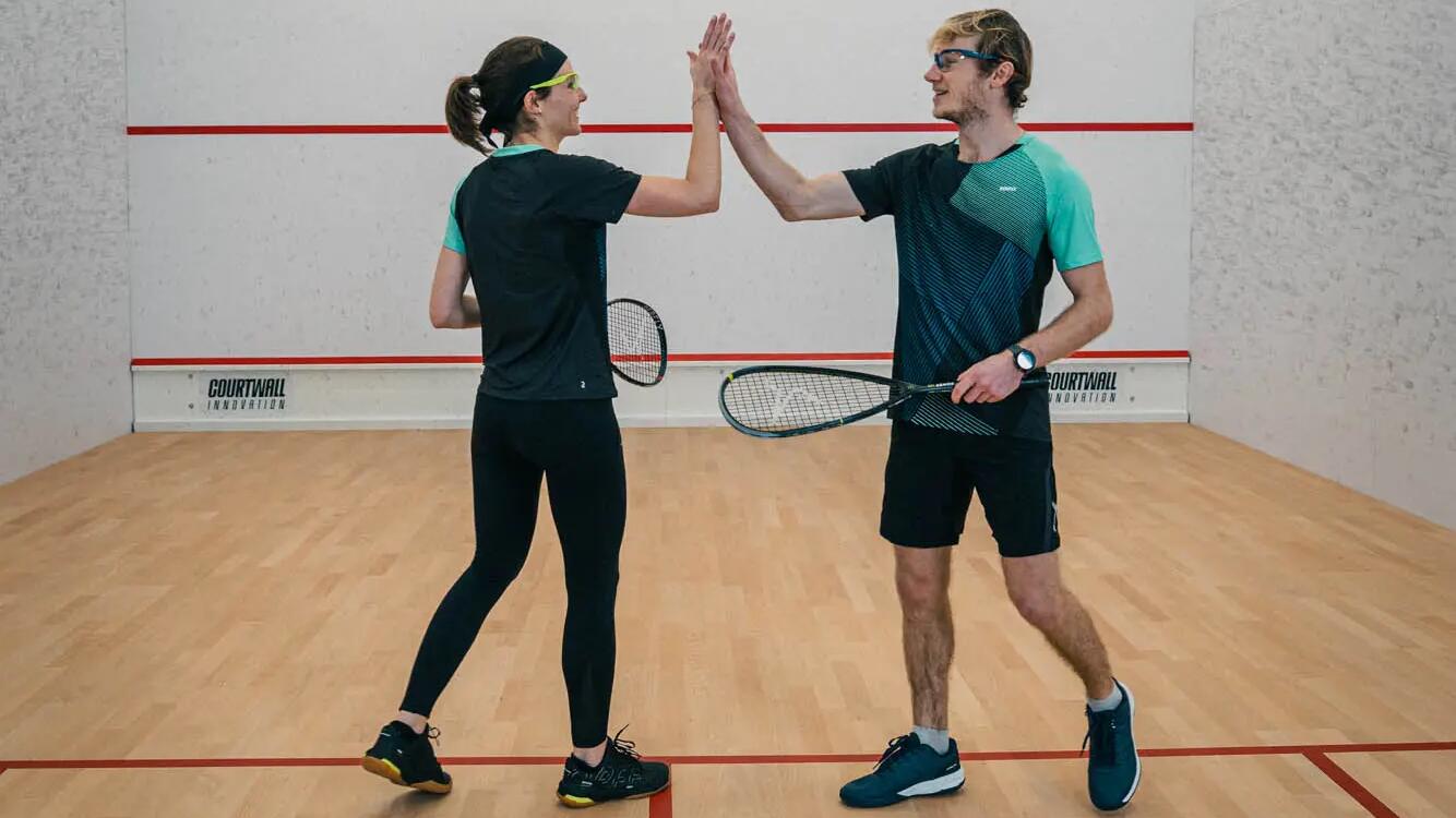 Eine Frau und ein Mann in Sportkleidung geben sich auf einem Squash-Court ein High Five.