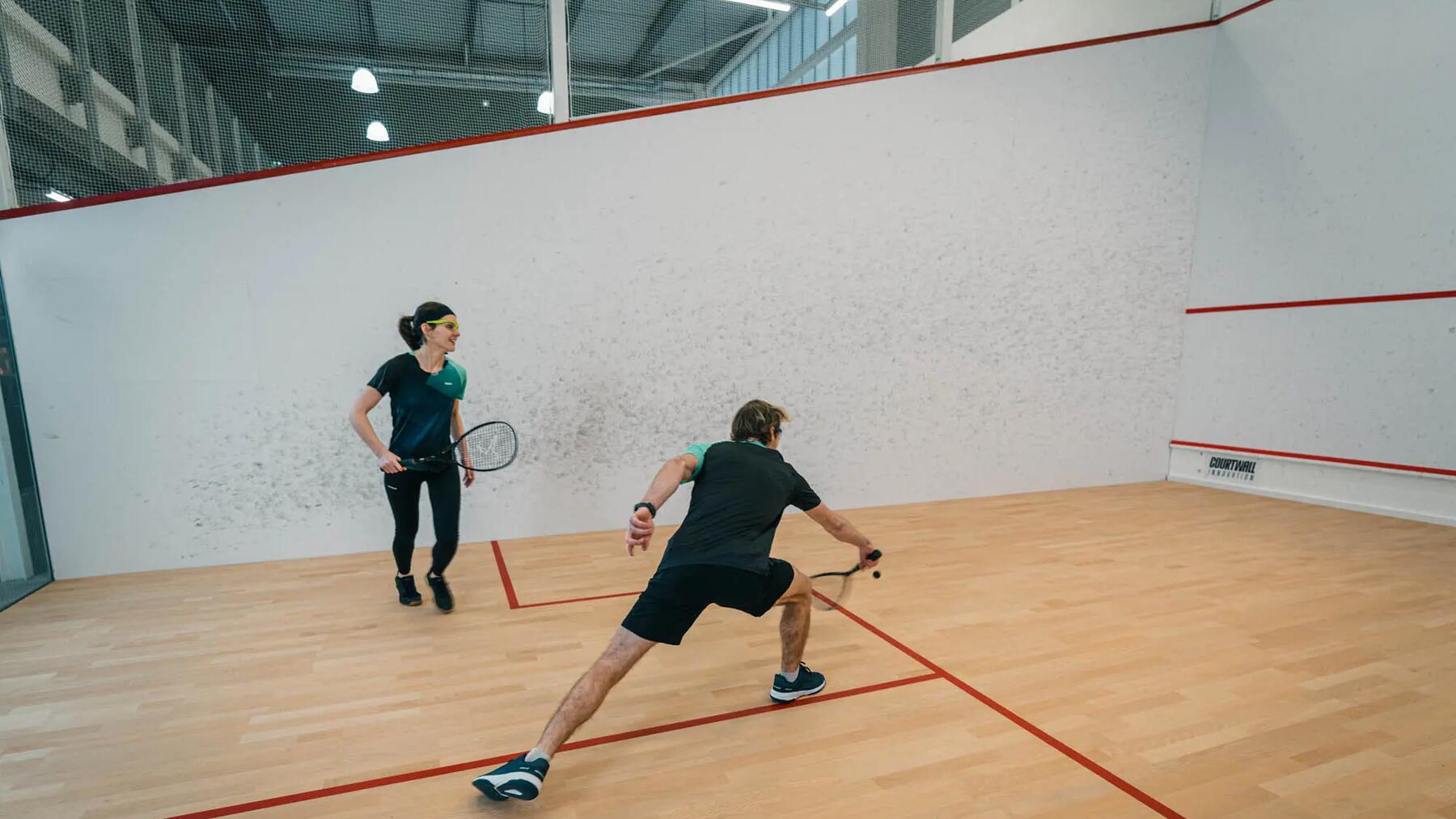 Ein Mann und eine Frau spielen Squash in einer hellen Halle.