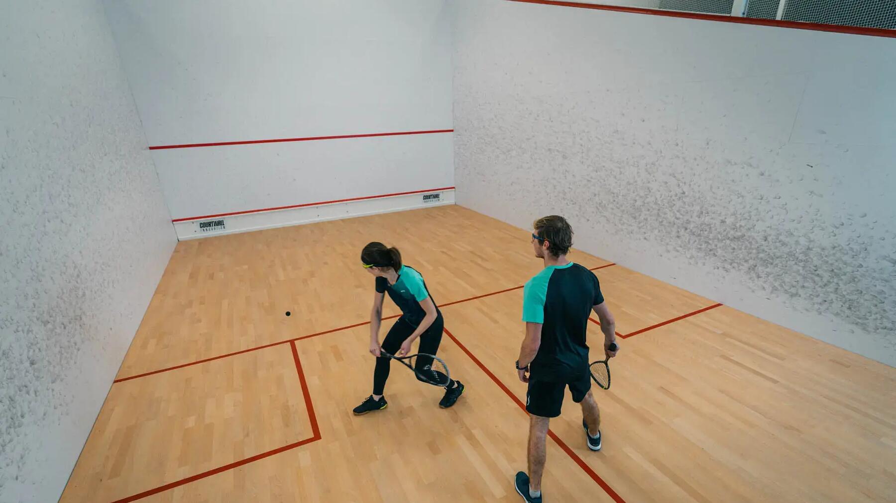 Ein Mann und eine Frau spielen Squash in einer hellen Halle.