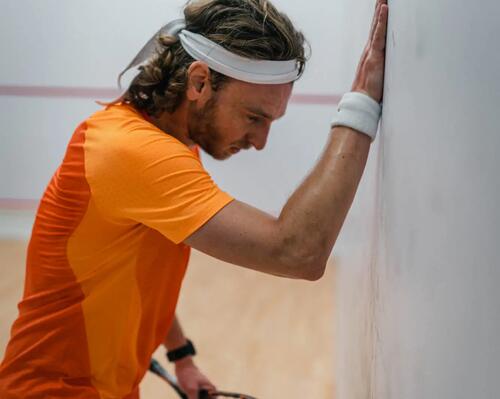 mężczyzna w stroju do squasha opierający się o ścianę