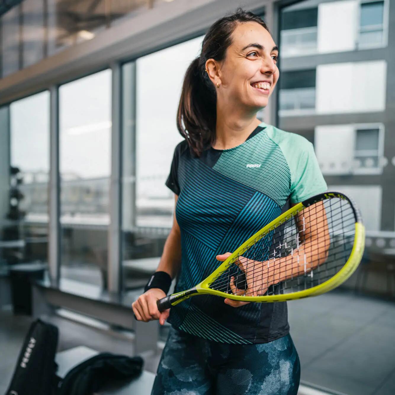 Uśmiechnięta kobieta w odzieży do squasha trzymająca rakietę do squasha