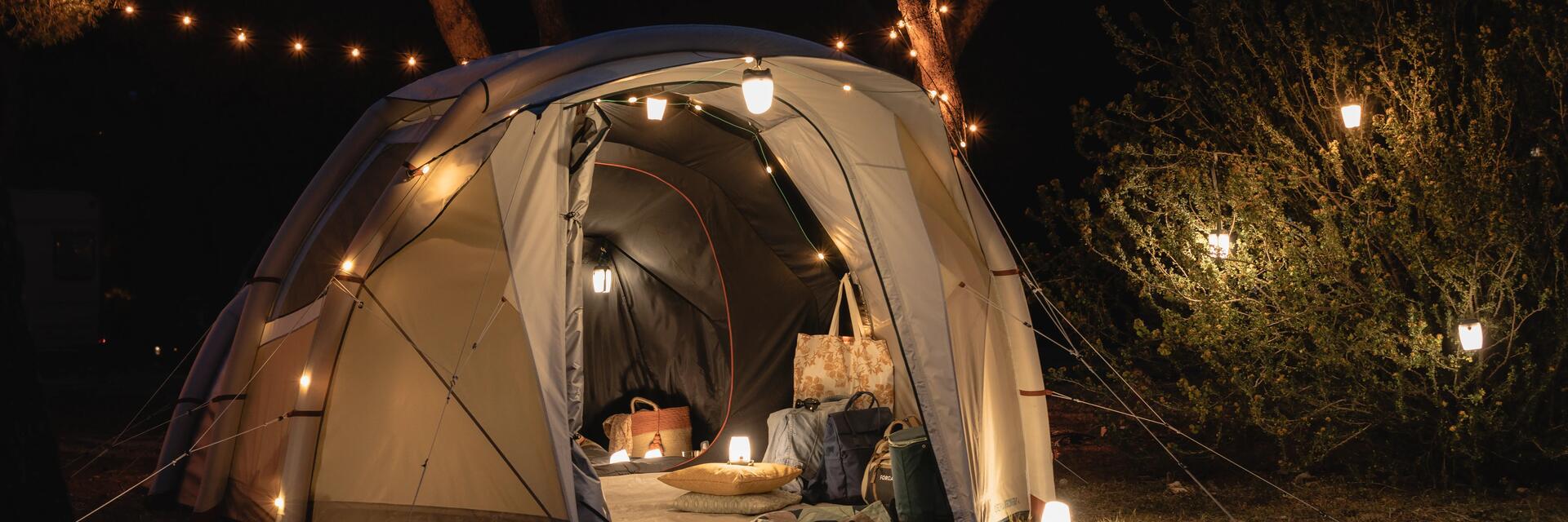 Namiot do spania na dziko z zawieszonymi lampkami  rozłożony w lesie nocą