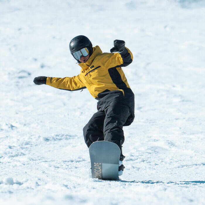 Snowboardista v žltej bunde na snowboarde Dreamscape