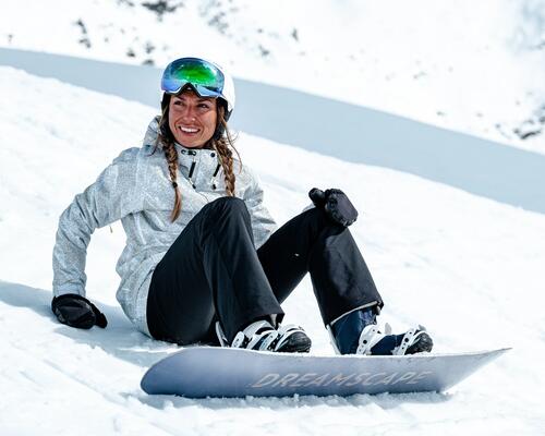 kobieta w stroju snowboardowym i przypiętą deską snowboardową siedzi na śniegu