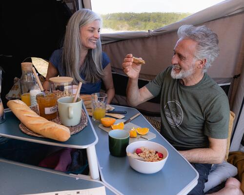 mężczyzna i kobieta spożywający posiłek w namiocie przy stoliku turystycznym