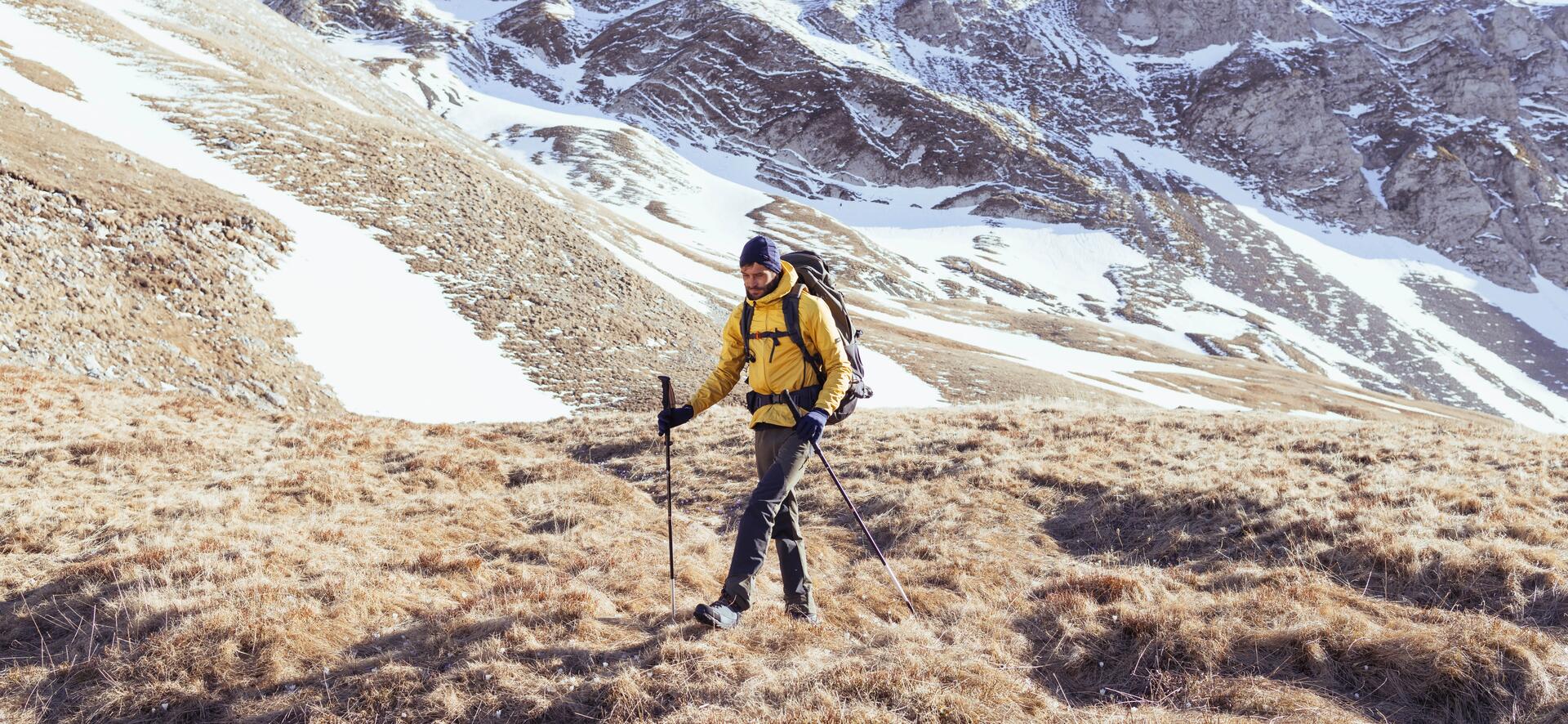 mężczyzna w odzieży trekkingowej wędrujący po górach zimą z kijami trekkingowymi 