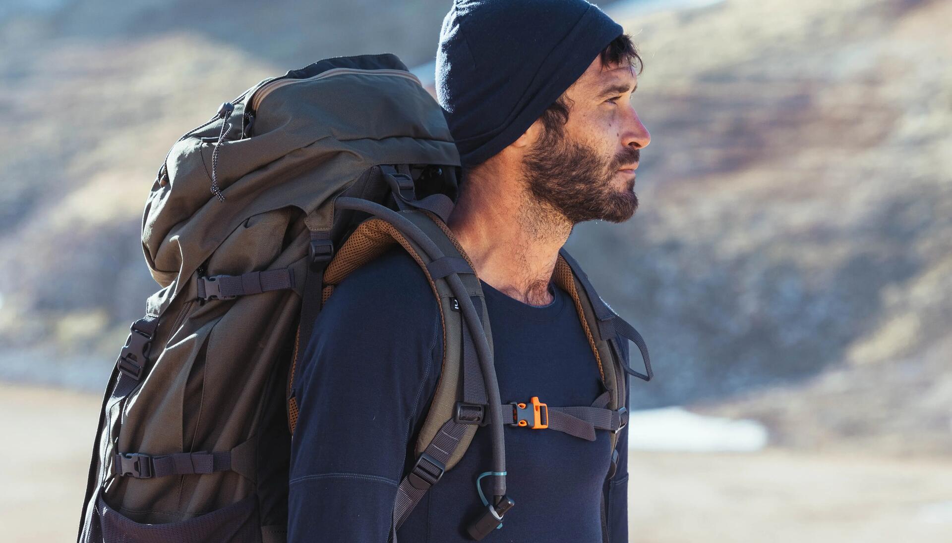 mężczyzna w czapce z plecakiem turystycznym na plecach stojący w górach