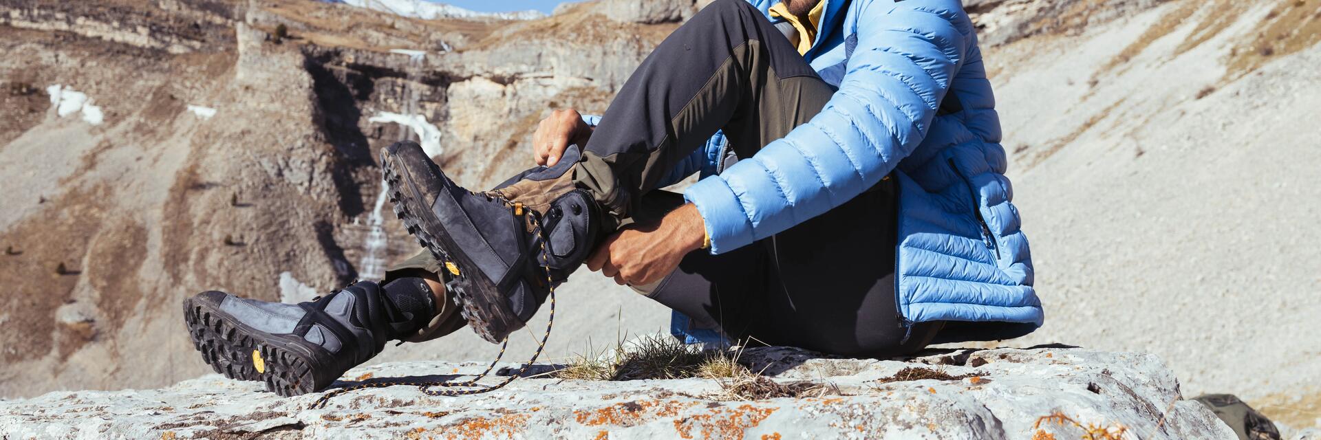 Mężczyzna ściągający buty trekkingowe z powodu powstania pęcherzy na stopach siedząc na kamieniu 