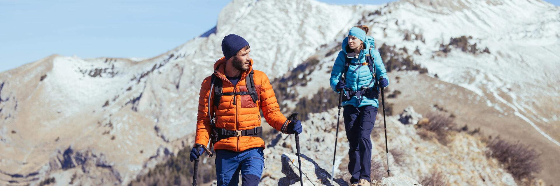 znajomi wędrujący z plecakami turystycznymi na plecach po górach w puchowych kurtkach trekkingowych