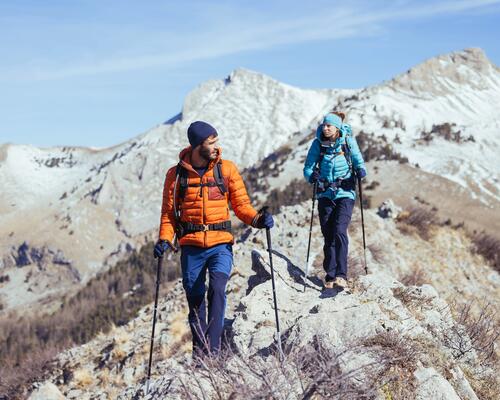 znajomi wędrujący z plecakami turystycznymi na plecach po górach w puchowych kurtkach trekkingowych