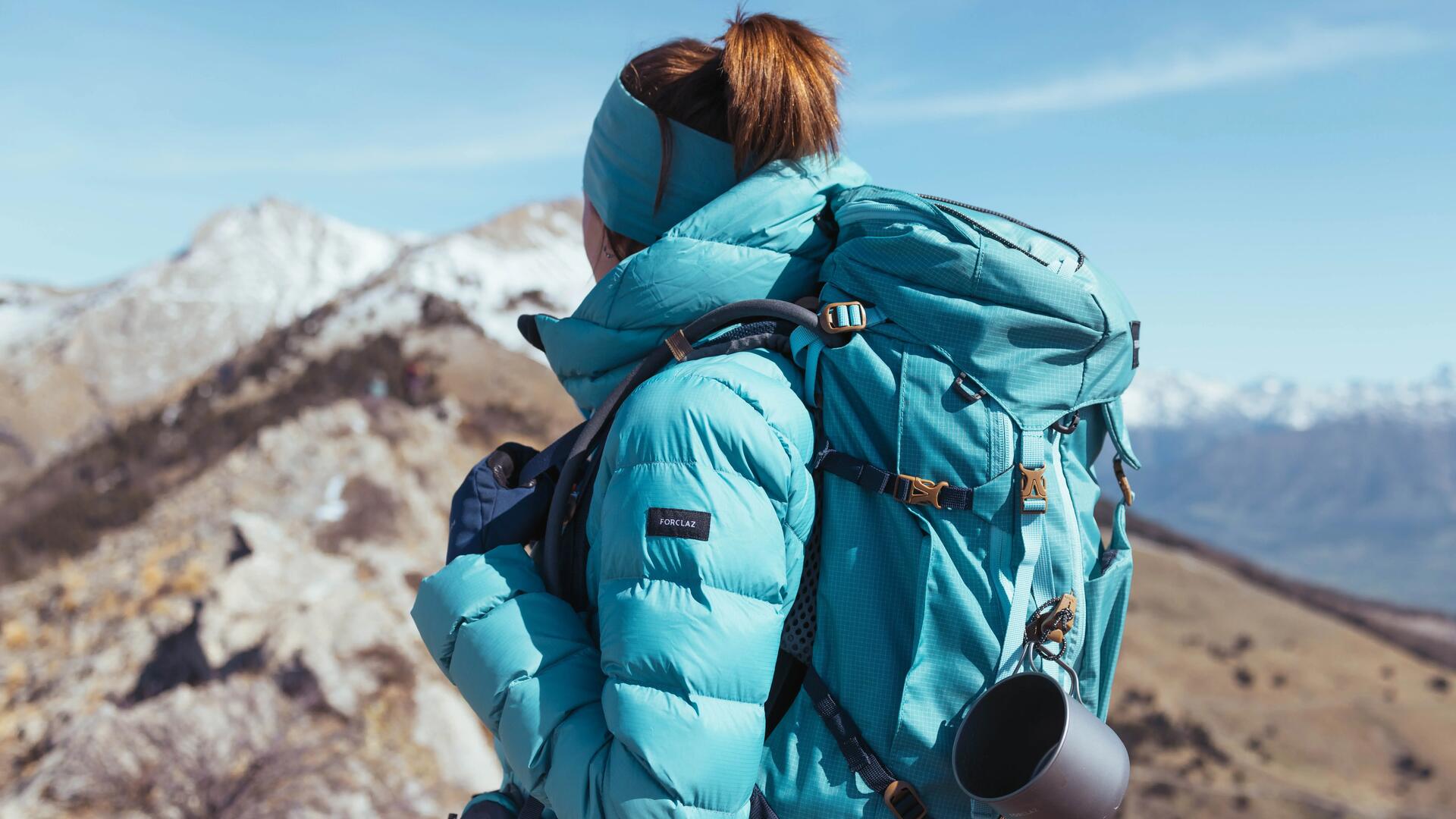 kobieta stojąca w górach w kurtce turystycznej z plecakiem turystycznym na plecach 
