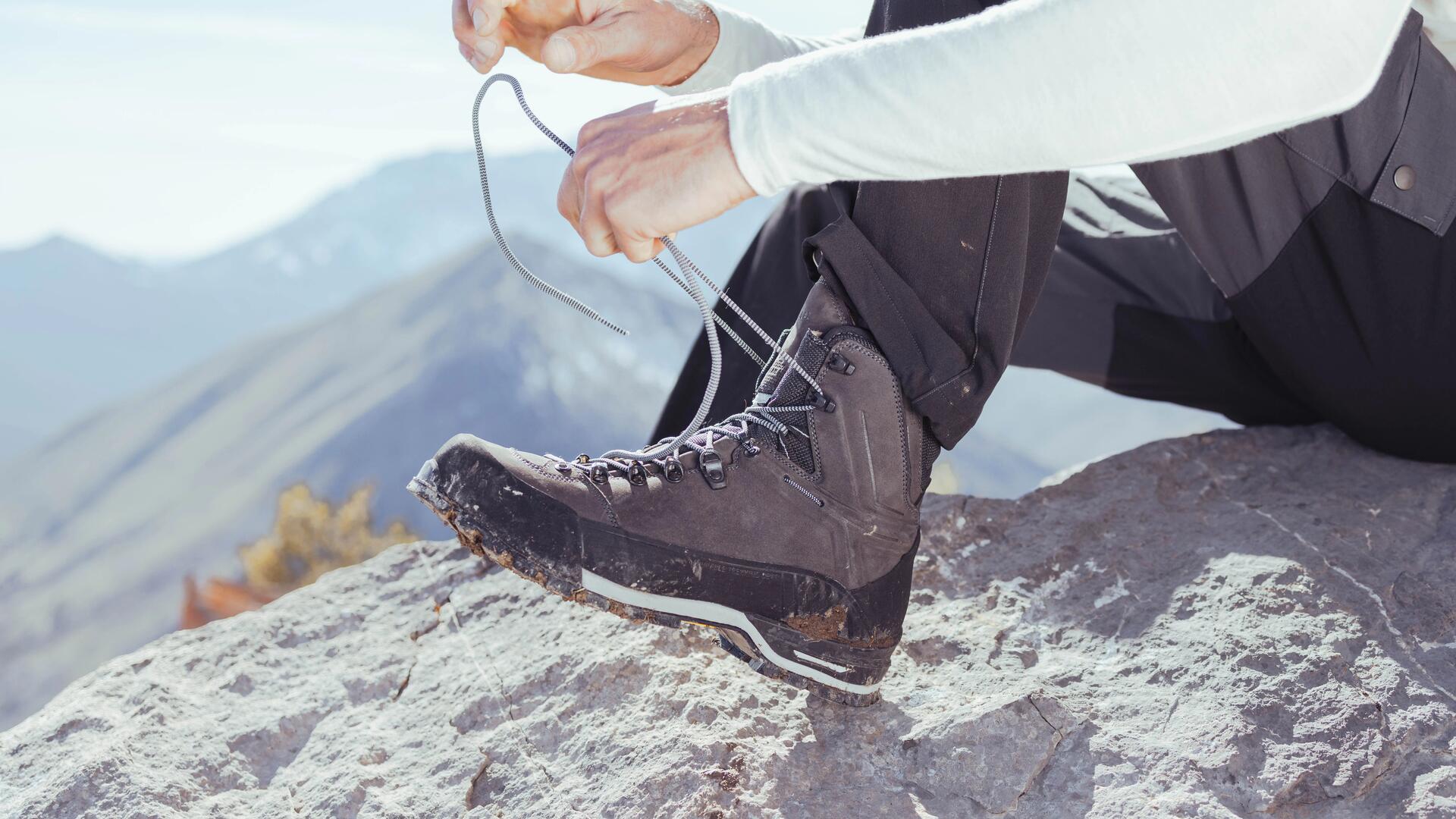 mężczyzna zawiązujący buty trekkingowe siedząc na skale