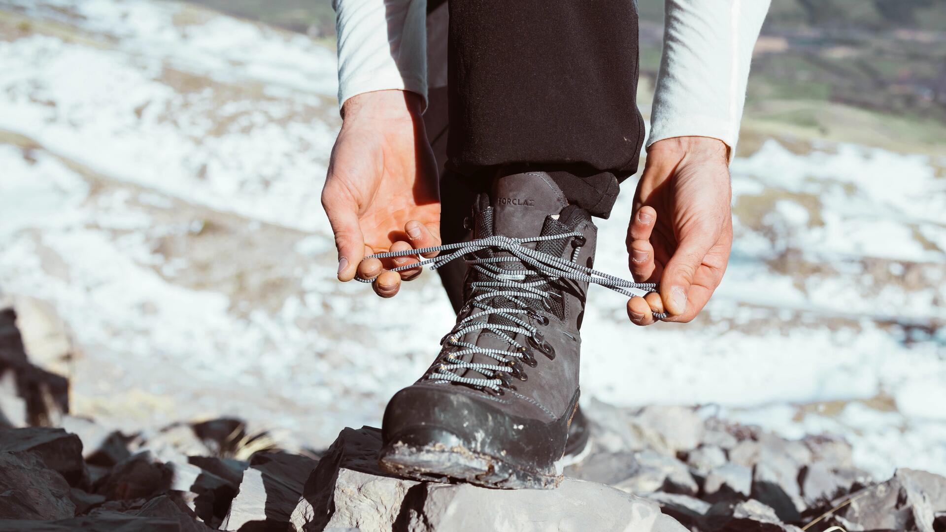 mężczyzna zawiązujący buty trekkingowe w górach