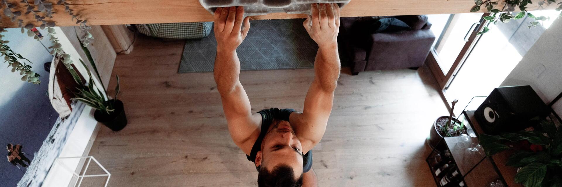Mężczyzna wykonujący trening wspinaczkowy przy użyciu chwytotablicy zamontowanej na belce w domu 