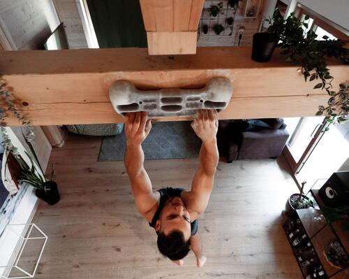 Mężczyzna wykonujący trening wspinaczkowy przy użyciu chwytotablicy zamontowanej na belce w domu 