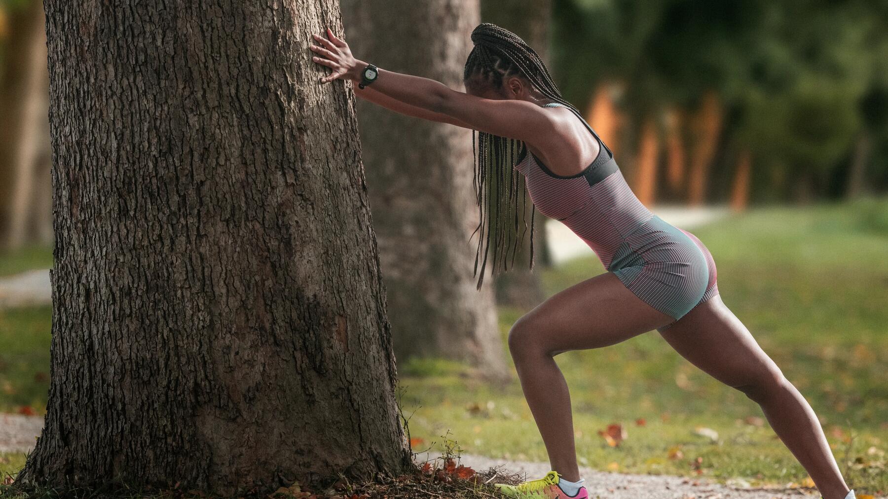 Eine Frau steht an einem Baum und macht dynamisches Dehnen