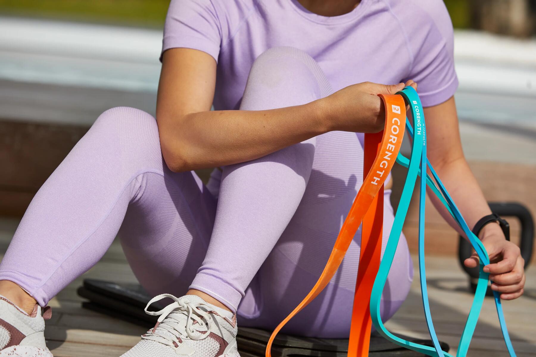 kobieta w odzieży fitness trzymająca gumy treningowe w różnych kolorach 