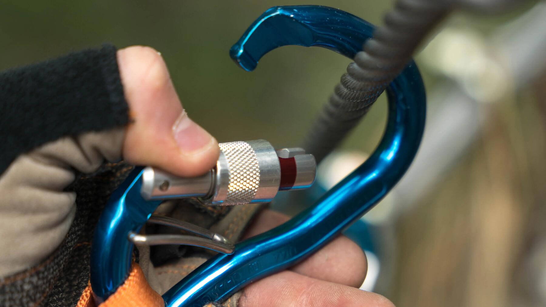 Person öffnet blauen Karabiner um diesen einzuhängen.