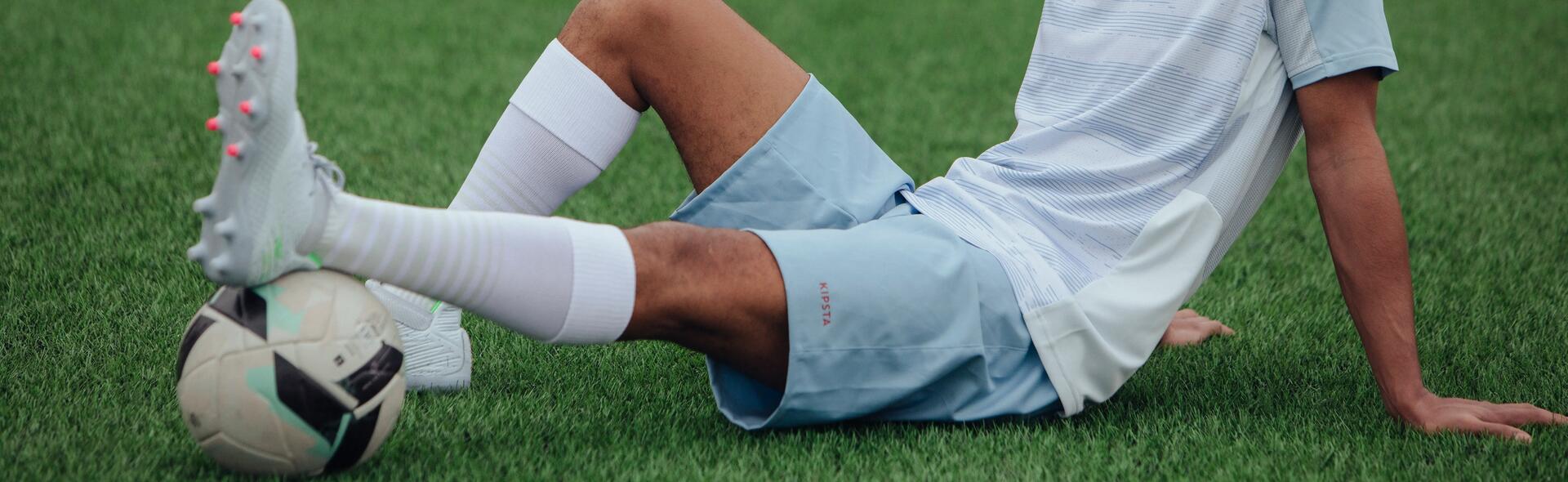 piłkarz siedzący na murawie w odzieży i butach piłkarskich