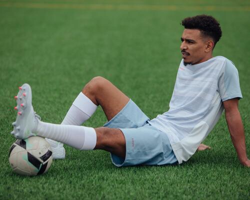 piłkarz siedzący na murawie w odzieży i butach piłkarskich