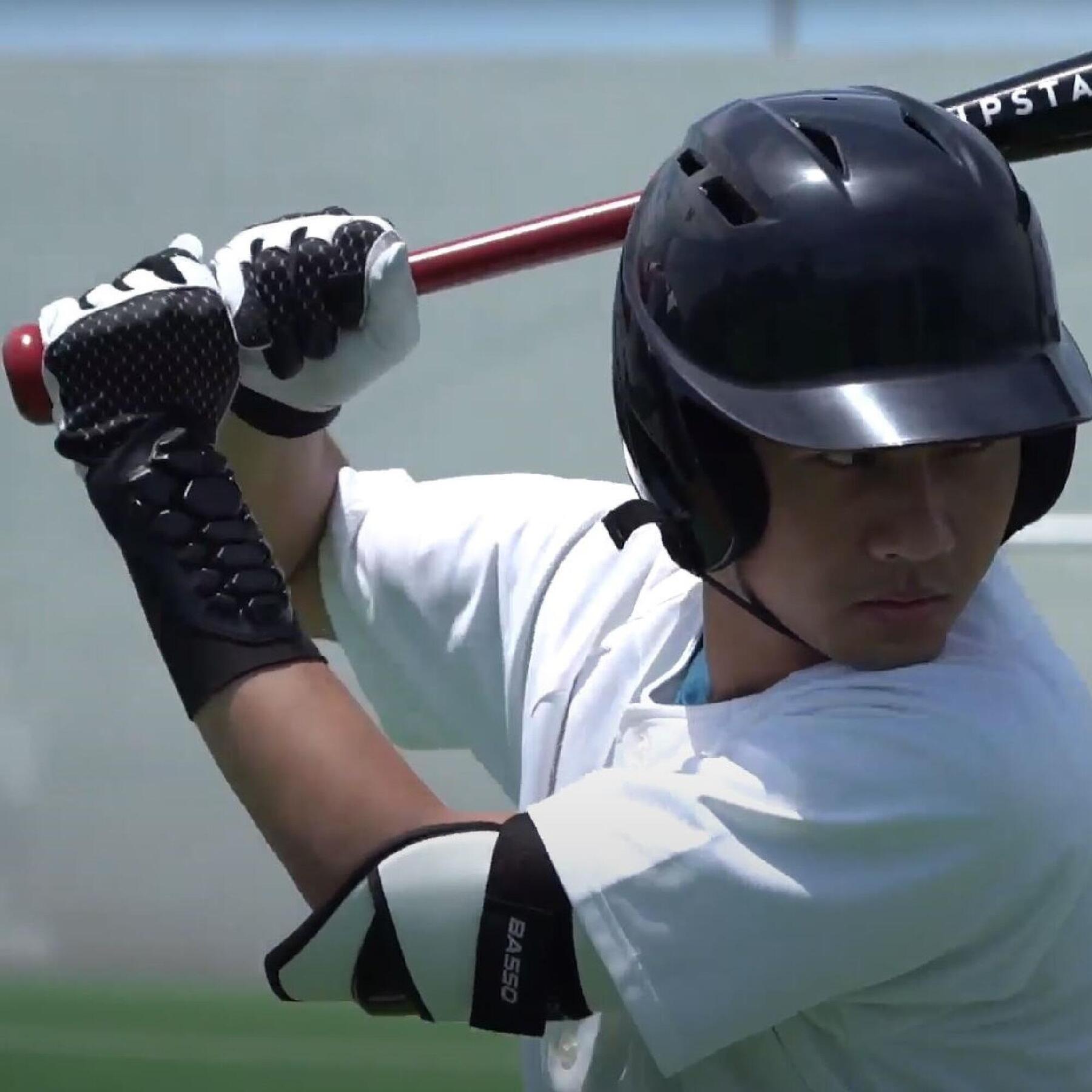 Zawodnik w rękawicach robiący zamach kijem baseballowym w kasku
