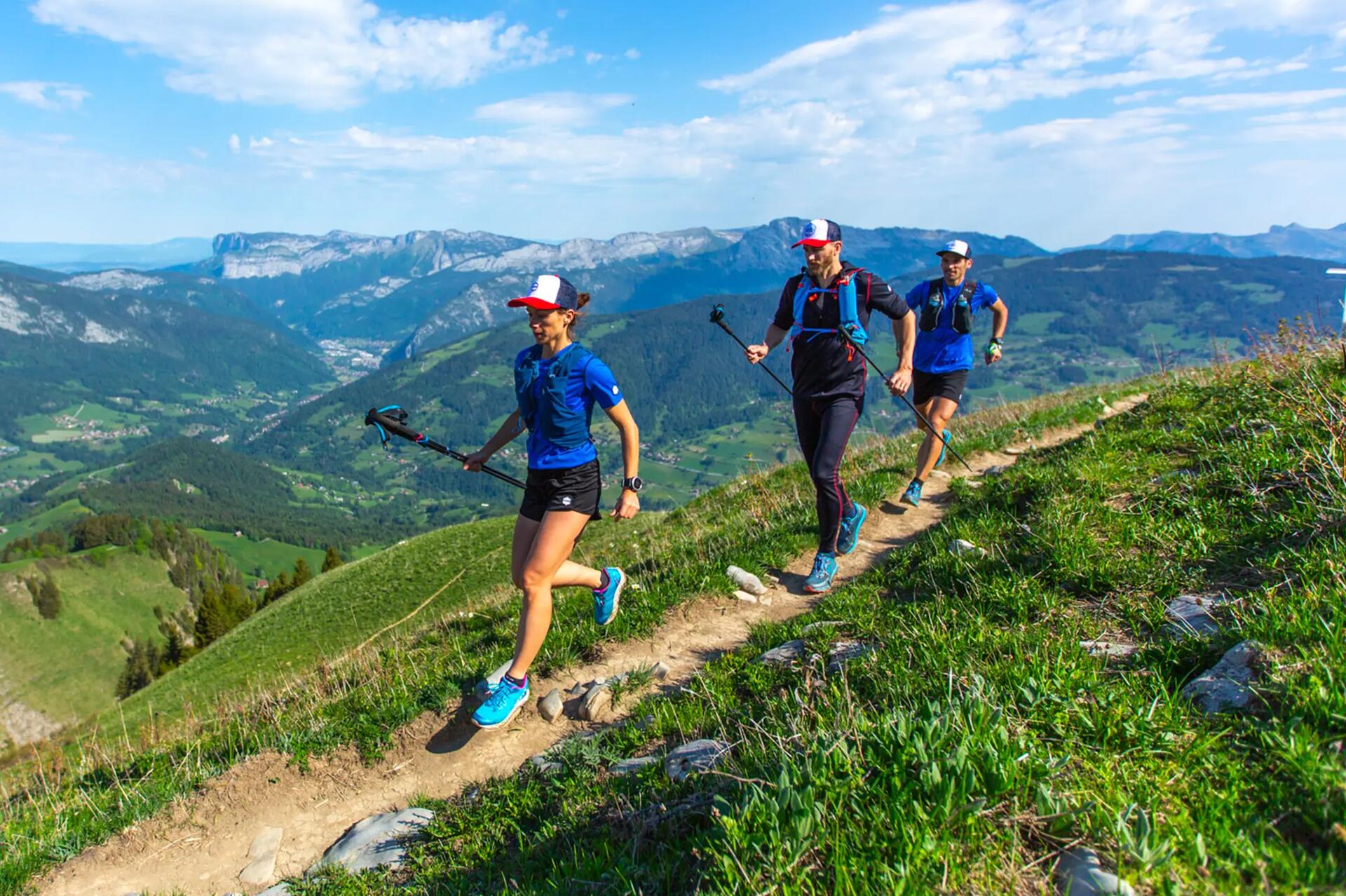 Kobieta i mężczyźni trenujący speed hiking na górskim szlaku z kijami trekkingowymi