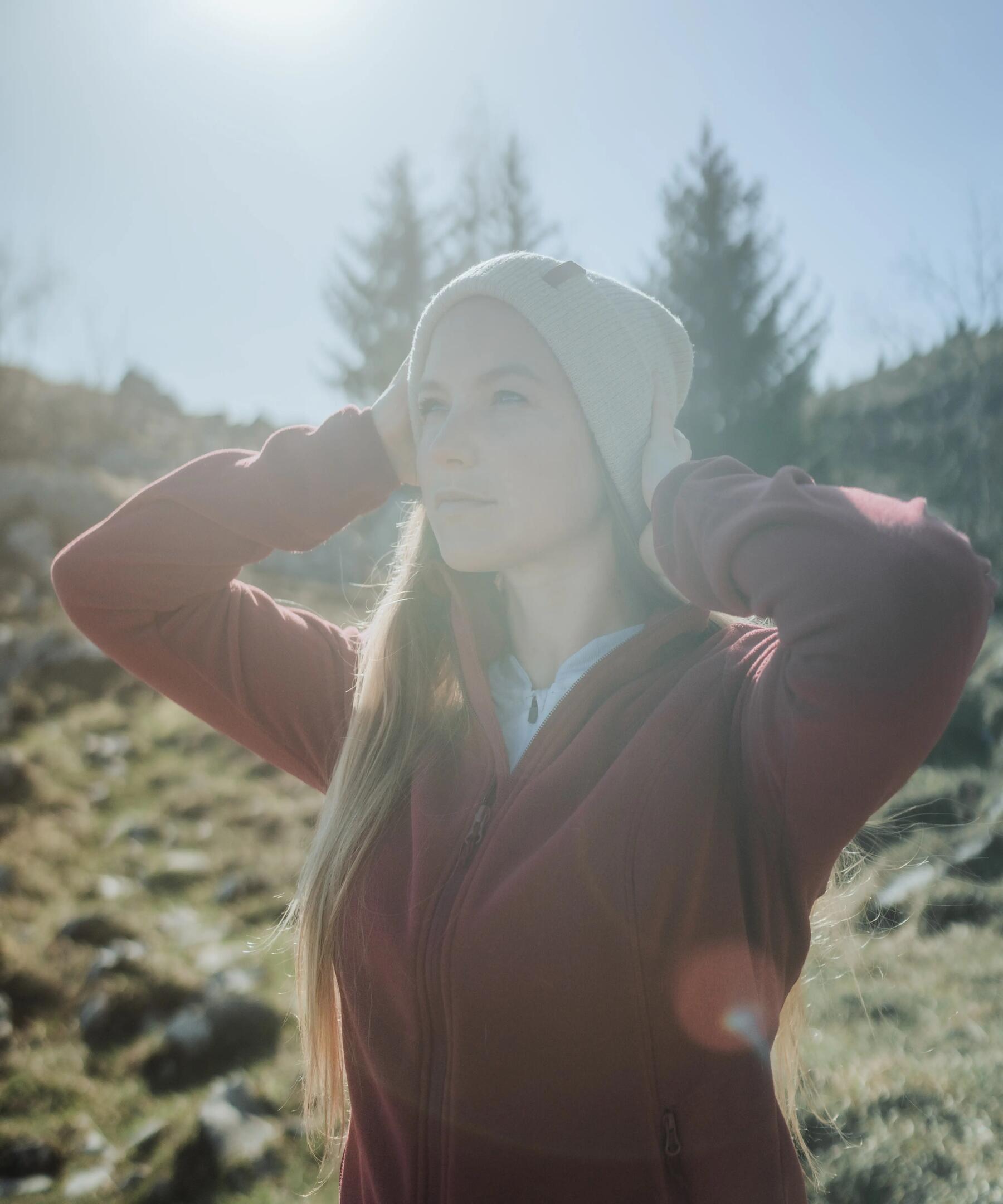 Kobieta stojąca w promieniach słonecznych w polarze i czapce zimowej