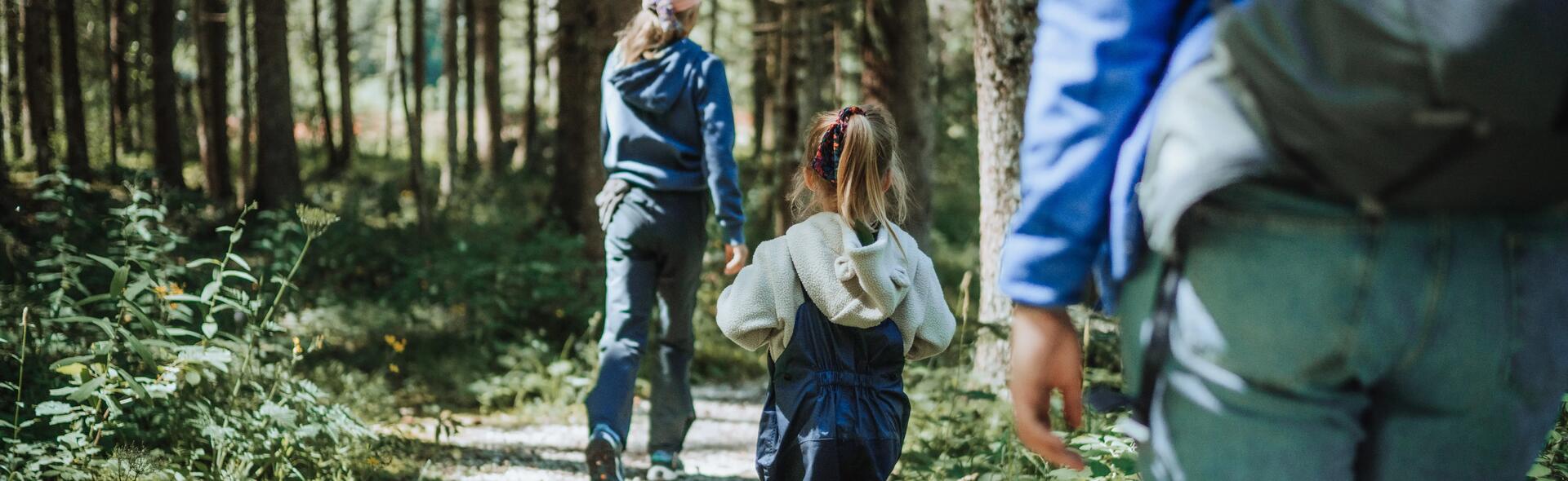 duas crianças e um adulto a caminhar numa floresta decathlon