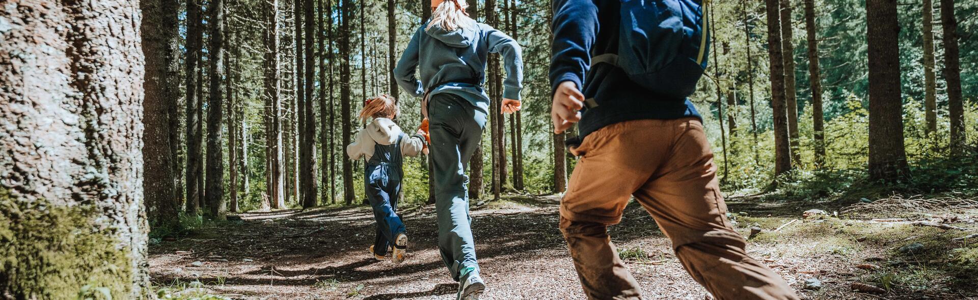 dzieci w odzieży trekkingowej biegnące przez las