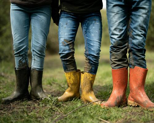 Close-up of three people wearing colourful wellies in muddy conditions