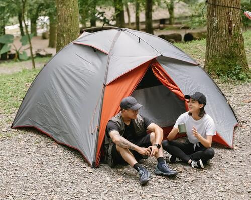 2 campers sitting outside their tent drinking and laughing