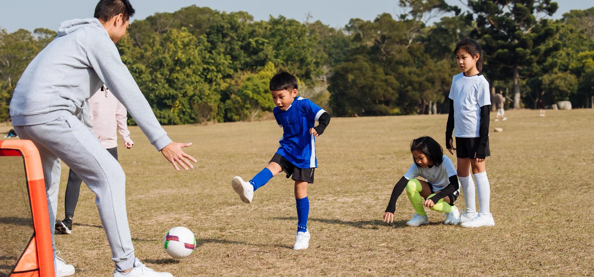 mężczyzna w dresie grający z dziećmi w strojach piłkarskich w piłkę nożną