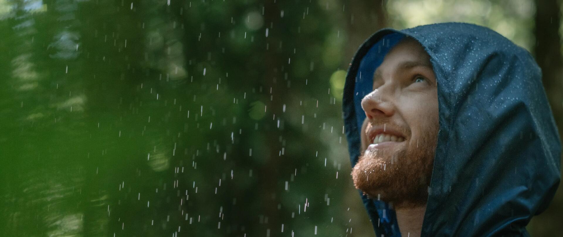 Mann in Regenjacke steht im Regen.