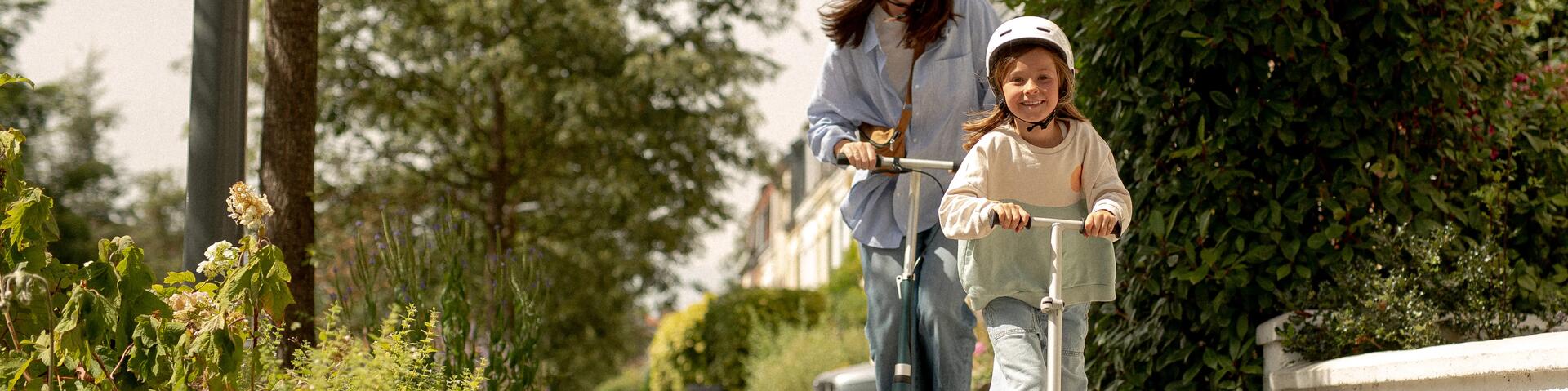 Young girl and mother riding on scooters outside