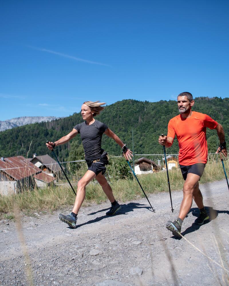 Ein Paar beim Nordic Walking auf einem Schotterweg vor Bergkulisse.