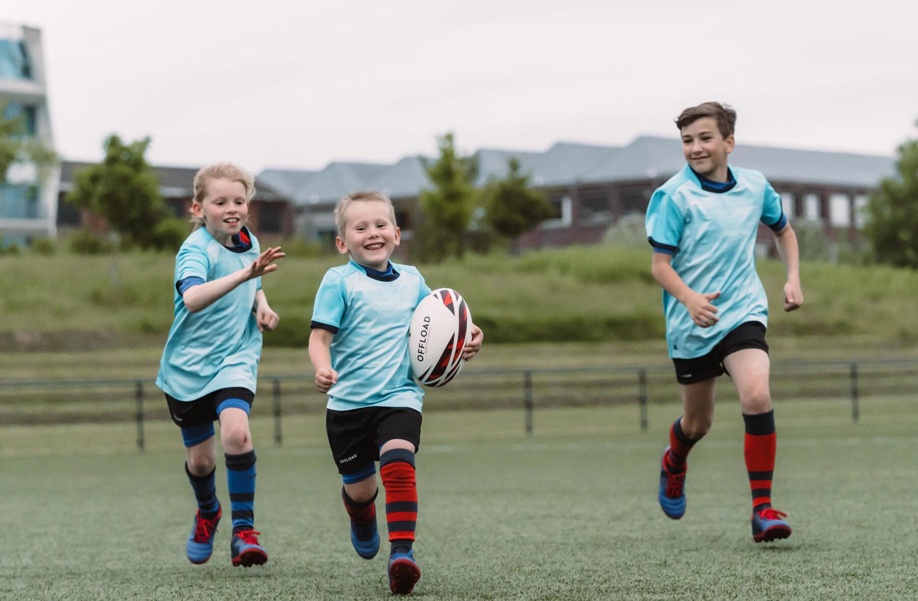 trójka dzieci w odzieży sportowej na boisku gra w rugby