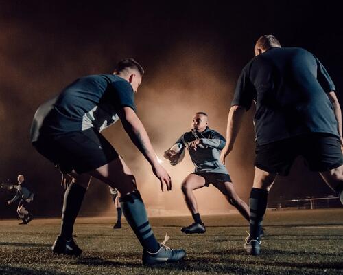 3 mężczyzn gra w rugby na boisku w strojach sportowych