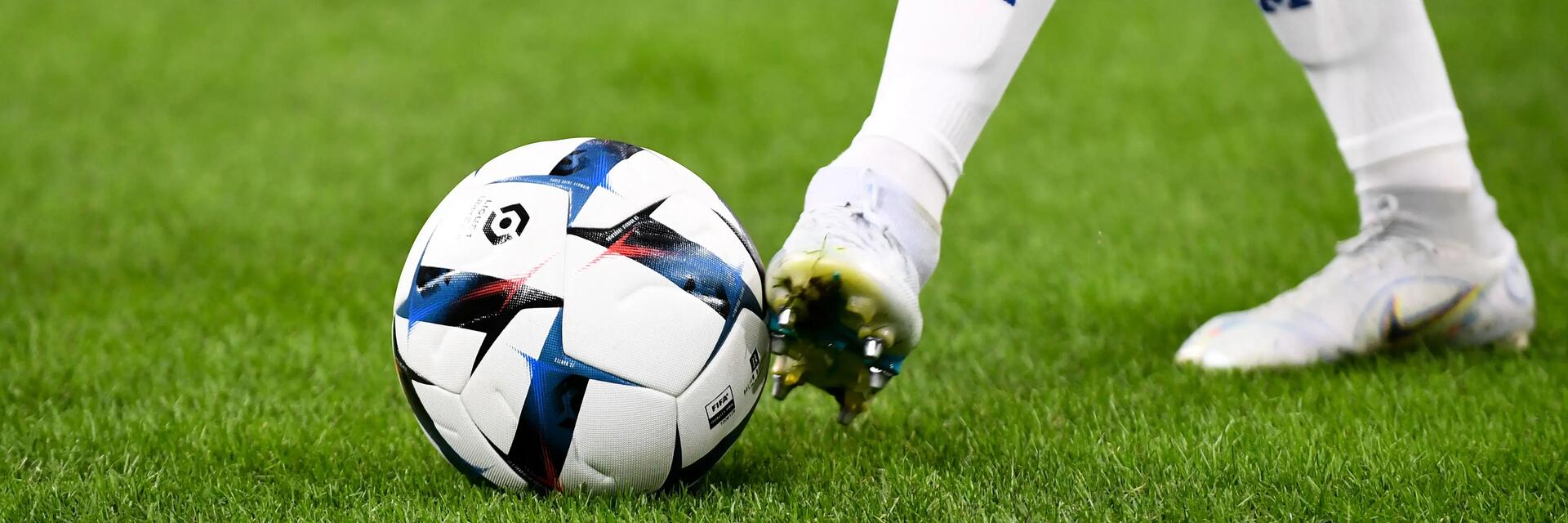 Piłkarz w korkach i getrach piłkarskich dotykający stopą piłki nożnej stojąc na murawie