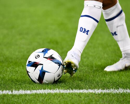 Piłkarz w korkach i getrach piłkarskich dotykający stopą piłki nożnej stojąc na murawie