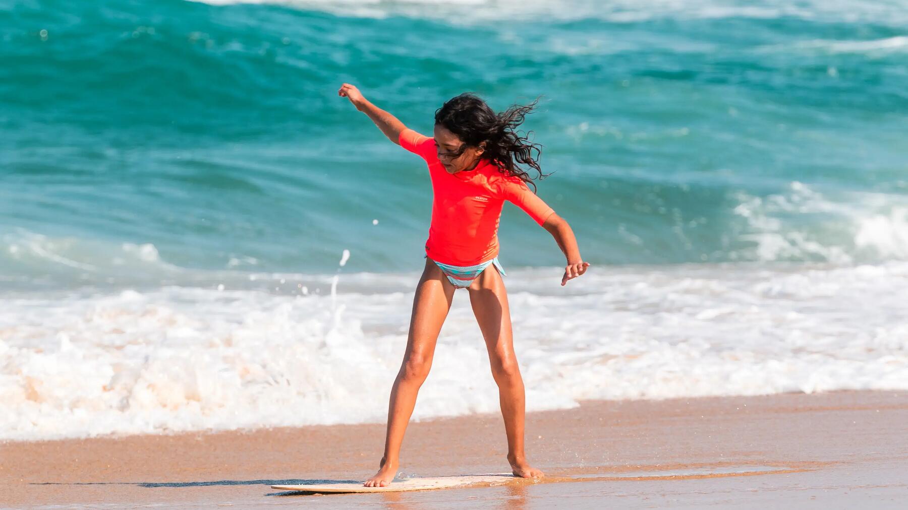 Dziewczynka przy brzegu stojąca na desce do skimboardingu