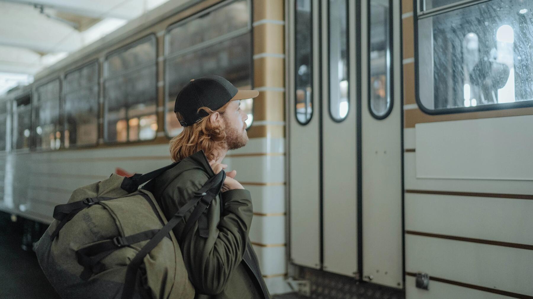 Mężczyzna z torbą turystyczną wybierający sie na city break stojąc przed wagonem pociągu