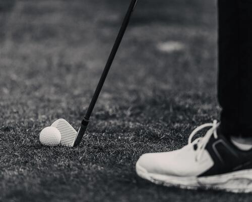mężczyzna w butach golfowych trzymający kij przy piłeczce golfowej